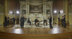 A group of string performers dressed in black play in a church